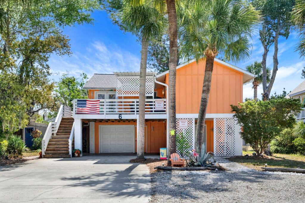 Front exterior of Tangerine Dream, a bright orange Coastal Empire vacation rental featuring palm trees, ample parking, and a large front deck.